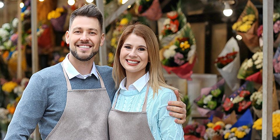 Young business owners, self employed, standing in front of their flower shop who are customers of a mortgage broker.