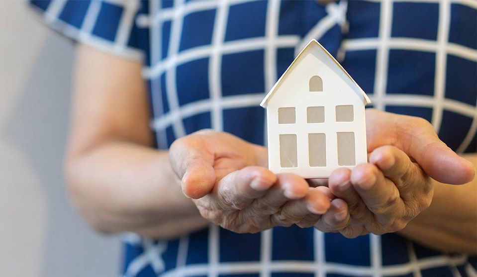 Woman in blue dress holding scale paper house cupped in her hands.