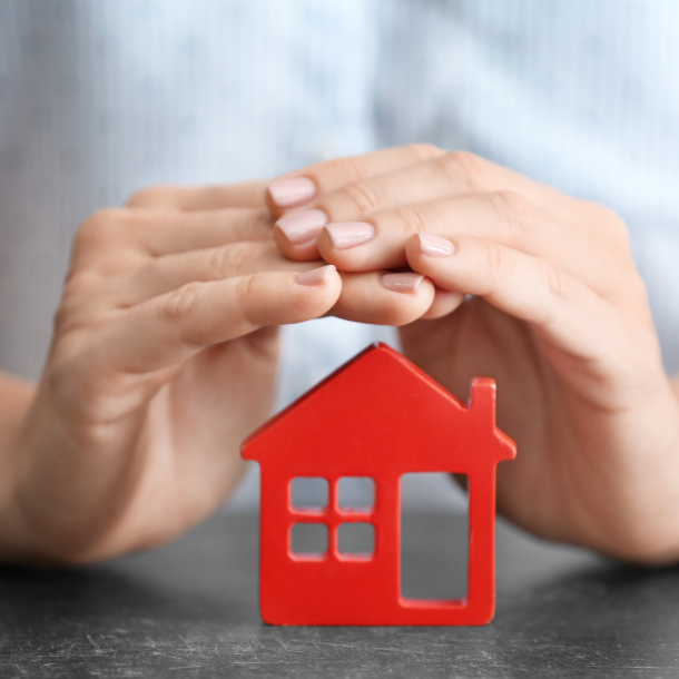 Hands cupped over a red cardboard cut out of a home showing that their new home loan will have mortgage insurance from a local mortgage lender.