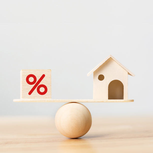 A light wood platform sits on top of a ball that with a light wood block with a red percentage symbol to the left and light wood home on the right. Showing balance by going to a mortgage lender.