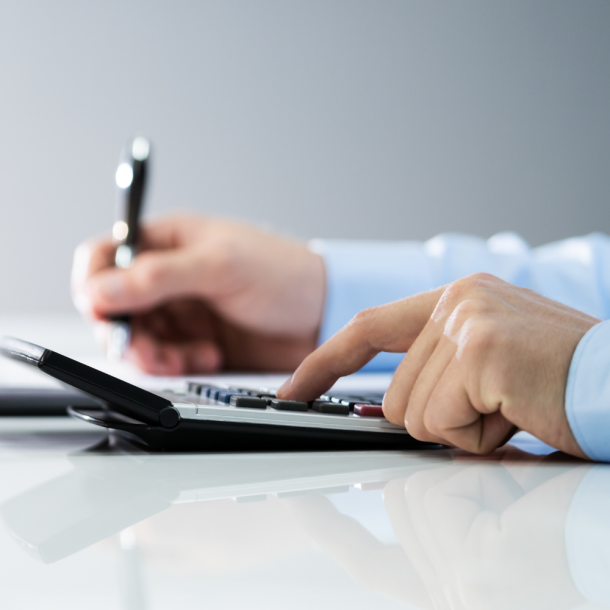 A customer's hands at a desk using a calculator in his left hand and a pen in his right hand determining mortgage rates from local mortgage lenders.