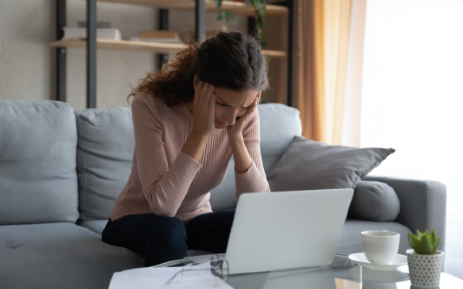 A woman sits in front of a laptop looking frustrated with her hands on her face weighing options between online-only lender and mortgage brokers.
